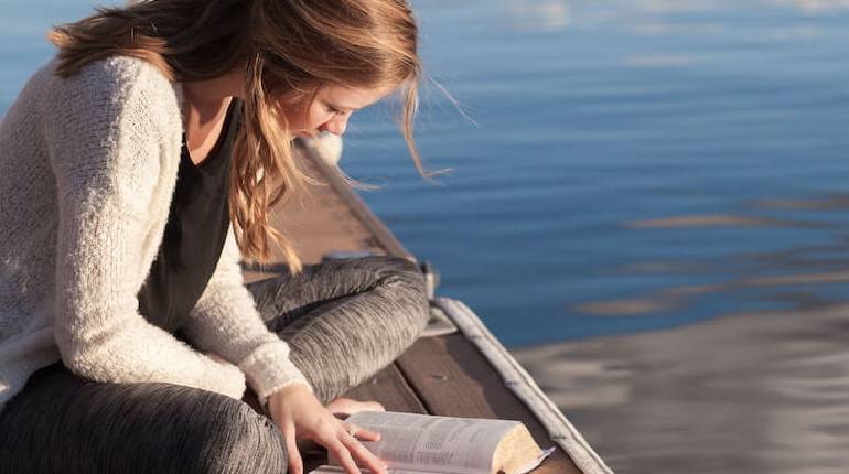 Image That Shows A Lady Reads a Book Sitting in a Beach